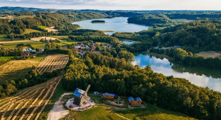 Malowniczy krajobraz kaszub z jeziorem, lasami, polami i drewnianym wiatrakiem.
