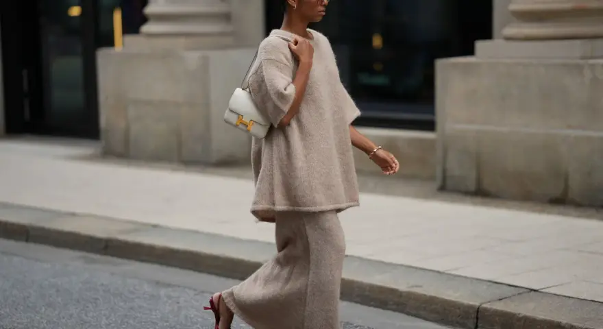 Donna con completo beige e borsa bianca, indossa scarpe rosse con tacco kitten, un dettaglio che aggiunge eleganza.
