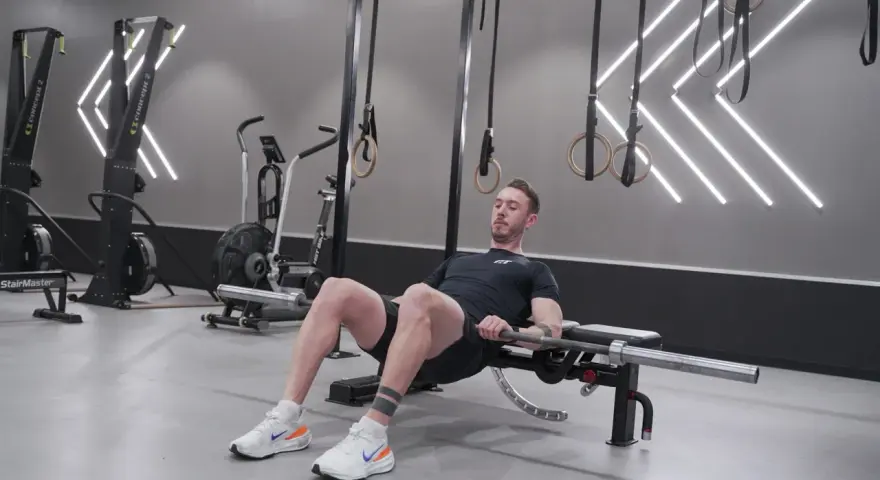 Man utför hip thrust med skivstång på en bänk i ett modernt gym.
