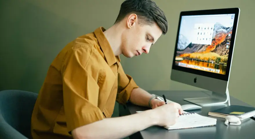 Student pracuje zdalnie, notując pomysły na komputerze. Idealna praca online dla studenta.