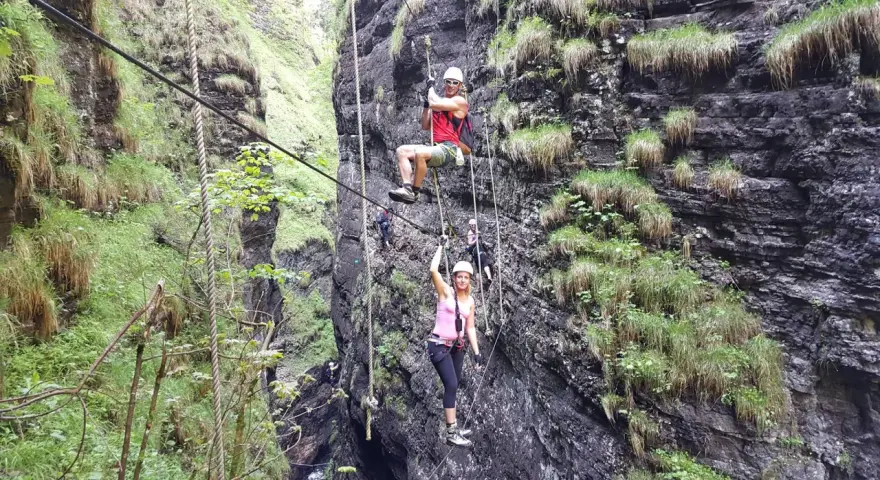 Abenteuer im **Postalmklamm Klettersteig**: Menschen seilen sich durch eine enge Schlucht ab, gesichert an Seilen, umgeben von steilen, bewachsenen Felswänden.