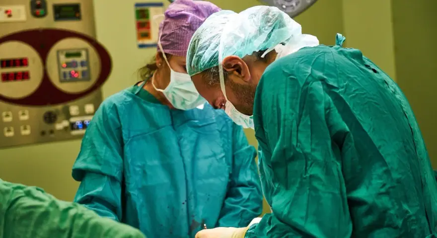 Chirurdzy w maseczkach i czepkach przygotowują się do operacji. Narkoza już działa, pacjent jest bezpieczny.