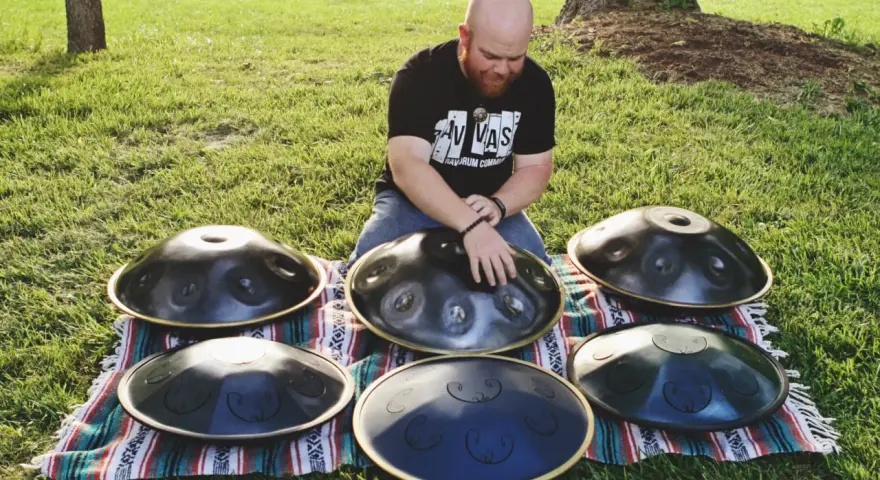 Mann spielt auf mehreren runden Metallinstrumenten im Freien.
