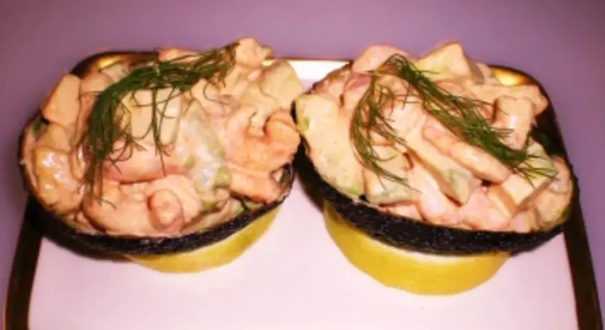 Zwei Avocadohälften gefüllt mit einem cremigen Krabbencocktail mit Avocado und Dill garniert, serviert auf Zitronenscheiben auf einem Teller.