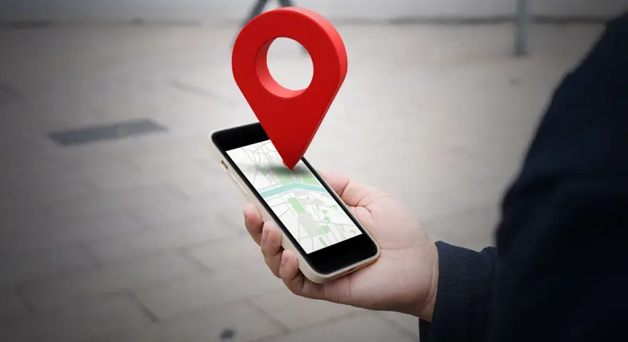 Dłoń trzyma smartfon z mapą, a nad nim unosi się czerwona pinezka. To wizualizacja, jak wysłać pinezkę z lokalizacją.