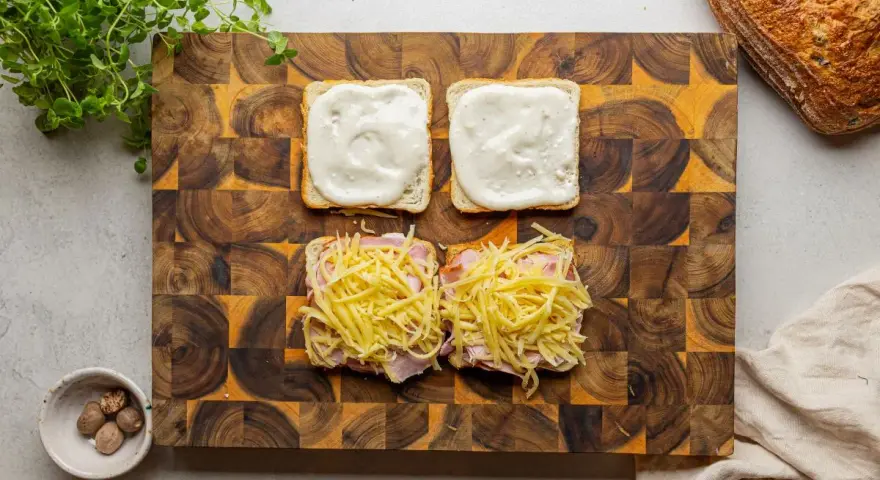 Przygotowanie croque madame: na kromkach chleba szynka i ser, na drugiej sos beszamelowy.