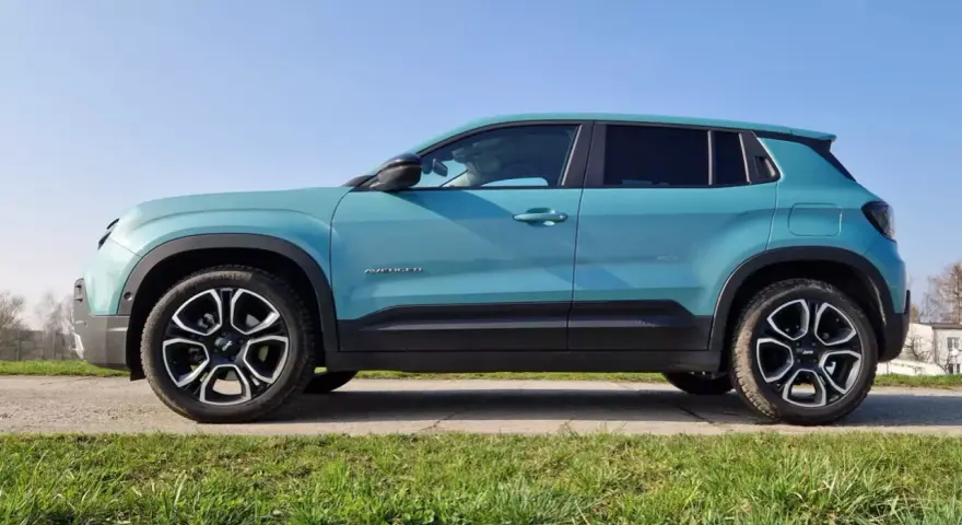 Turkusowy Jeep Avenger 4x4 z czarnymi felgami na tle nieba i trawy.