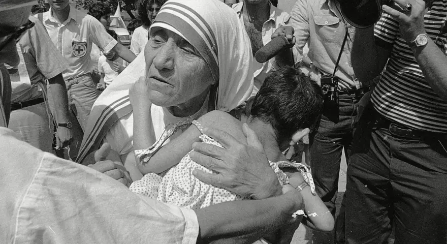 Missionaries of Charity founder, Mother Teresa, cradles a child amidst a crowd and media attention.
