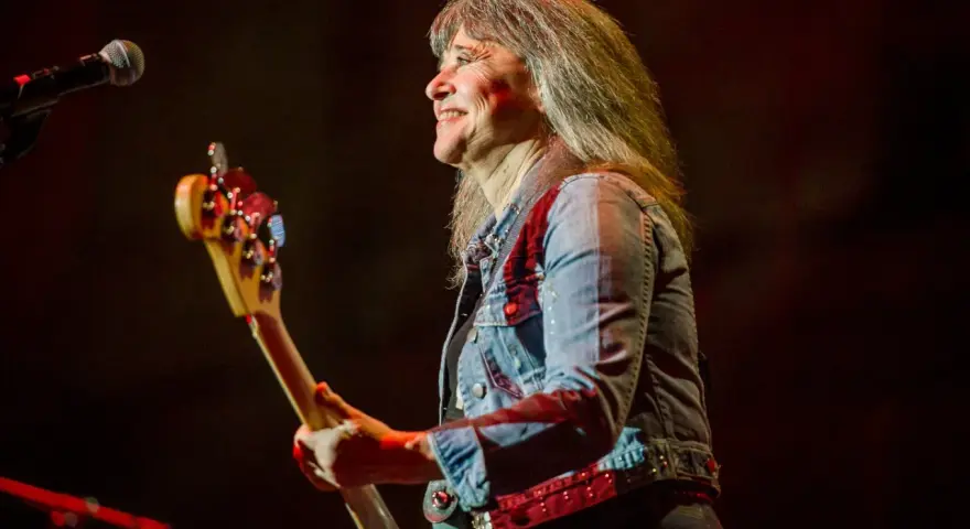 Suzi Quatro dzisiaj na scenie, z basem w ręku, uśmiecha się do publiczności. Rock'n'rollowa legenda w dżinsowej kurtce.