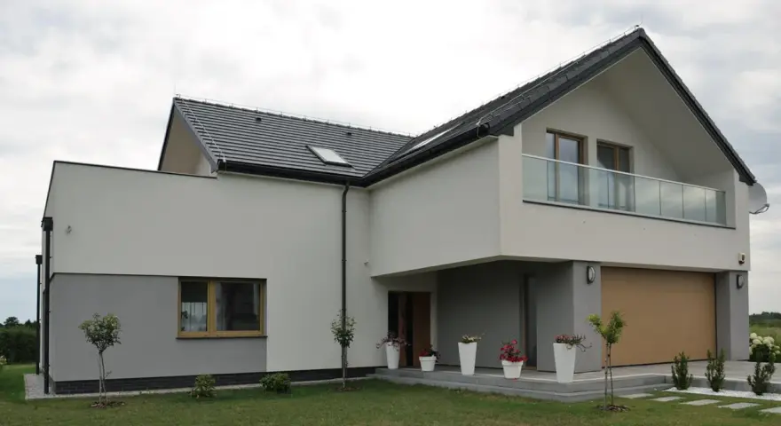 Nowoczesna elewacja domu z szarymi i białymi tynkami, dużym garażem i balkonem z przeszkloną balustradą.