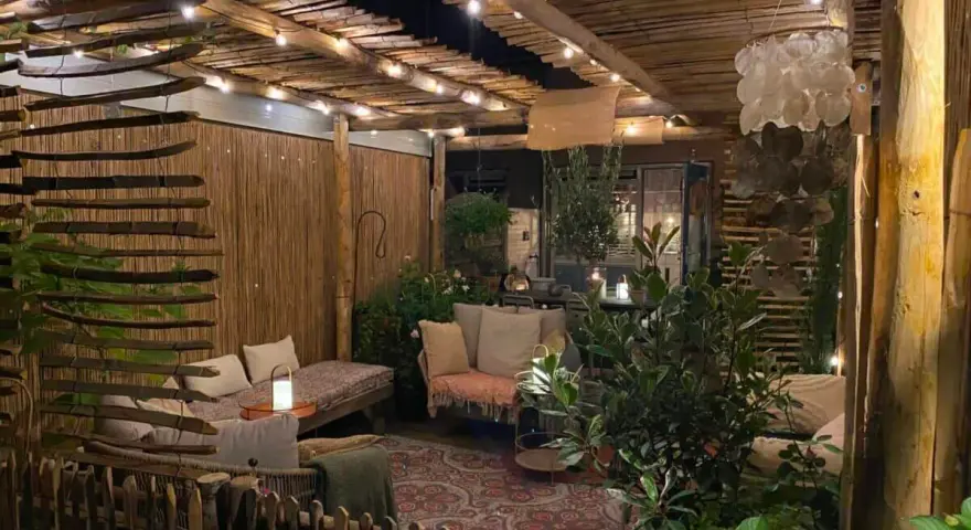 Une terrasse de jardin aménagée en coin cocooning, avec des banquettes confortables, des lumières douces et une ambiance chaleureuse.