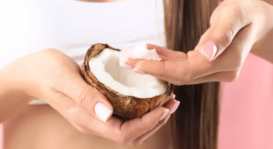 Mani con unghie curate prendono polpa di cocco da una noce, ingrediente perfetto per una maschera capelli fai da te nutriente.
