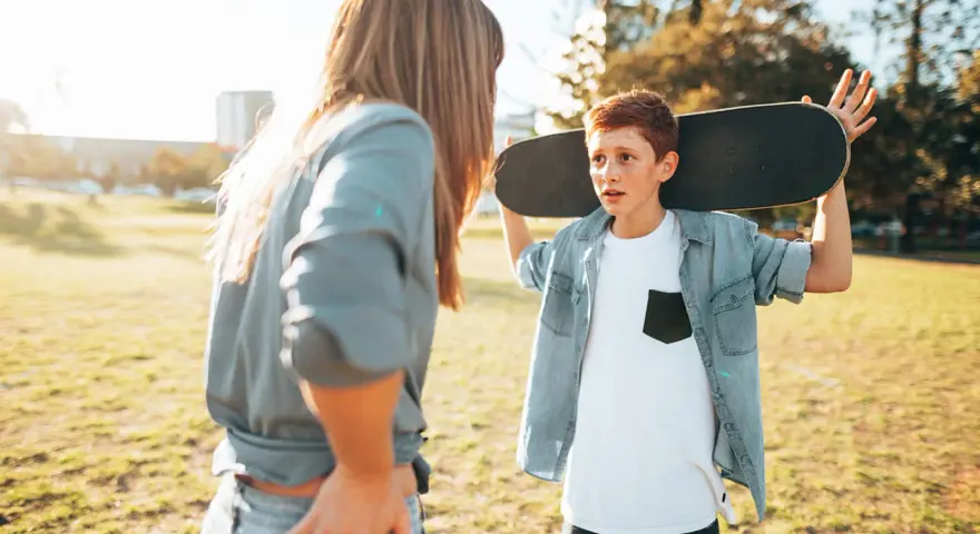 Ein Junge mit einem Skateboard über der Schulter spricht mit einer Frau. Die **Adoleszenz** ist eine spannende Zeit voller Entdeckungen.