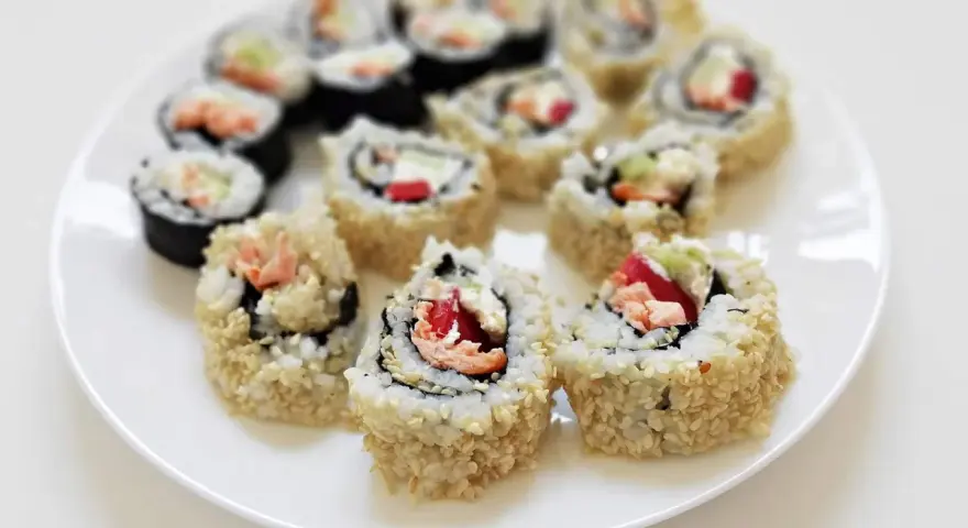 Talerz pełen sushi uramaki z łososiem, awokado i papryką, posypane sezamem. Pyszne i kolorowe rolki.