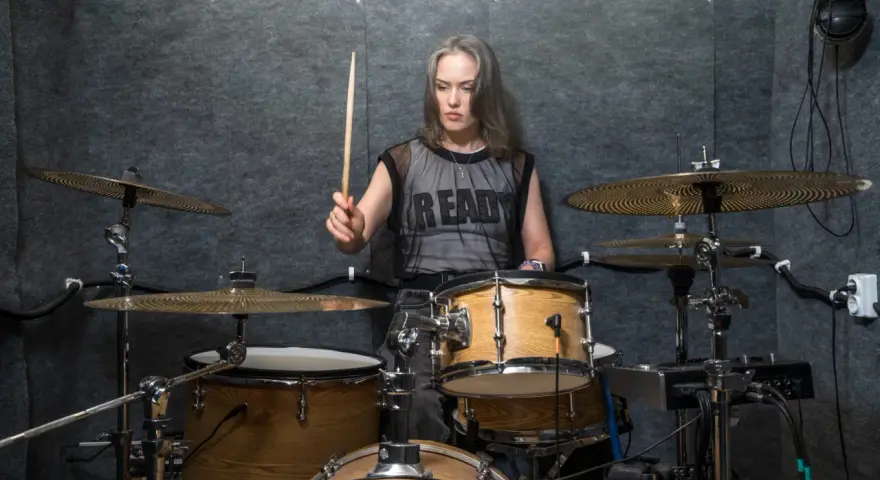 Kobieta z pałeczką w dłoni, gotowa do wygenerowania mocnych **drum beats** na zestawie perkusyjnym w studio.