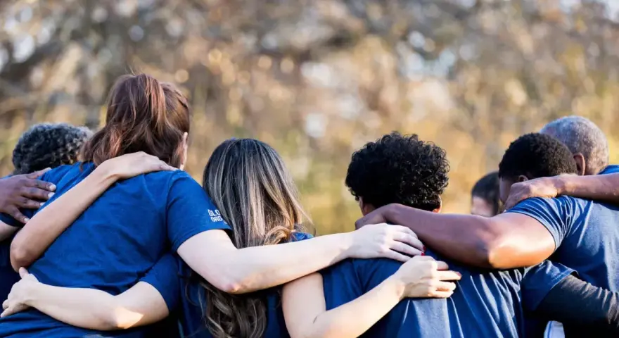 A diverse group of people in blue shirts huddle together, arms around each other, symbolizing collaboration and the strength of revenue diversification.