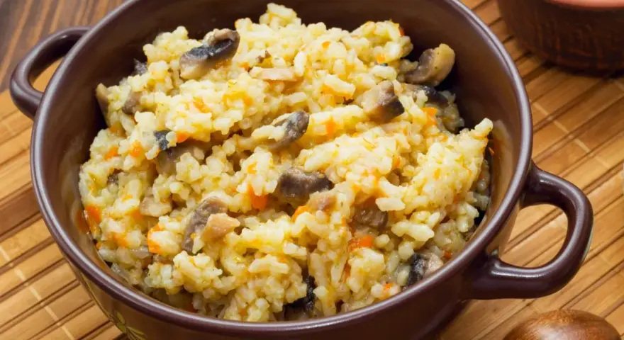 Kremowe risotto z grzybami i marchewką w brązowej misce, obok drewniana łyżka.