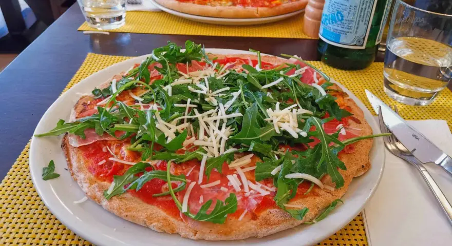 Leckere Pizza mit Rucola und Schinken auf einem Teller, ein Beispiel für glutenfreie Restaurants.
