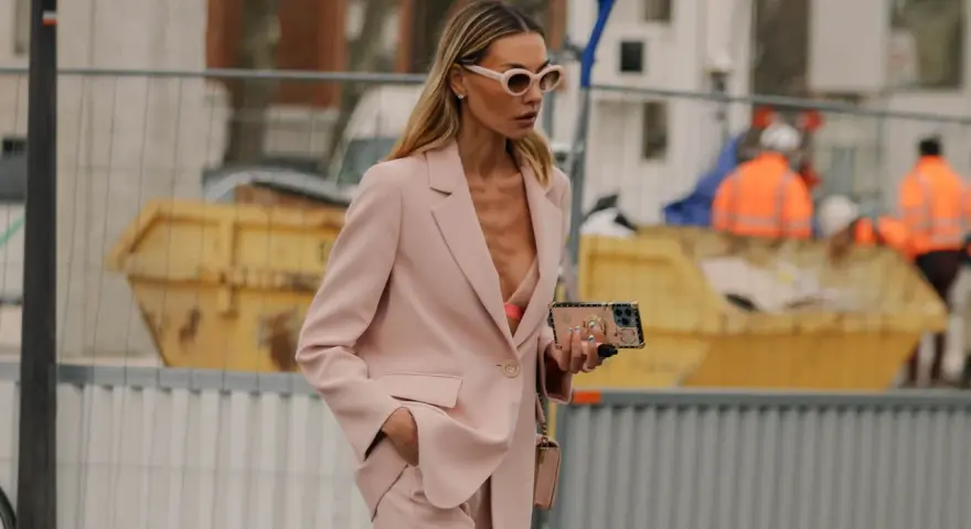 Donna con tailleur rosa, reggiseno a vista e occhiali da sole. Un look chic per ogni occasione.