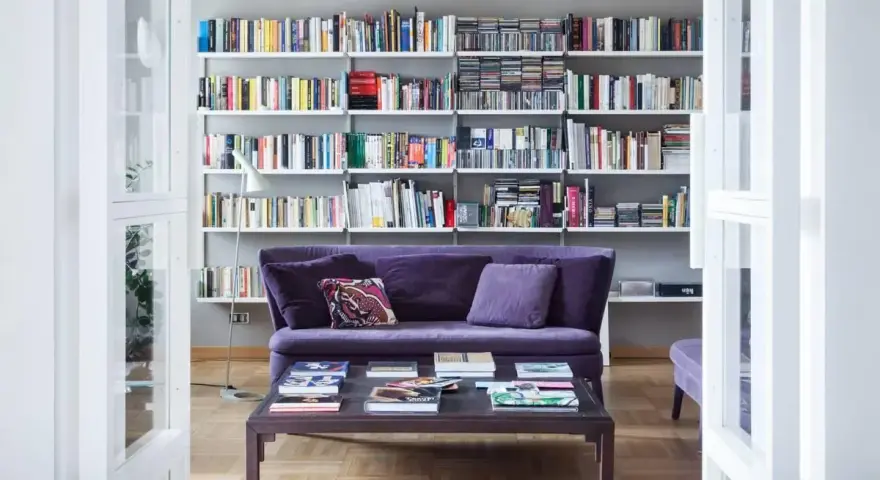Un divano viola accogliente davanti a una libreria bassa piena di libri e CD.