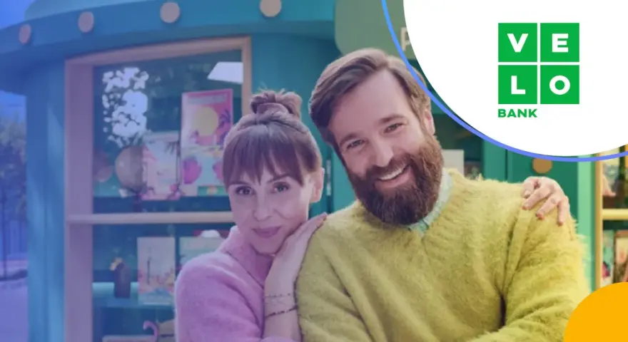 Uśmiechnięta para przed budką z logo Velo Bank. Dowiedz się, velo bank co to za bank i jakie ma oferty.