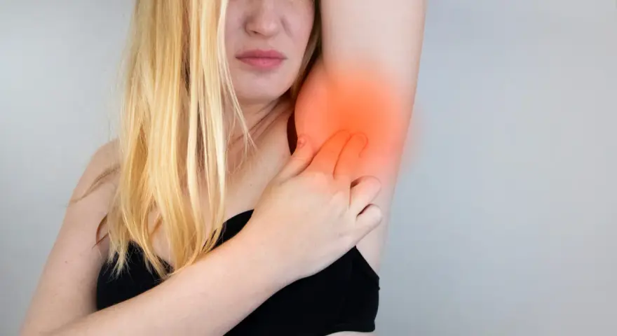 Kobieta z blond włosami odczuwa ból po usunięciu węzłów chłonnych, dotykając bolącej pachy.