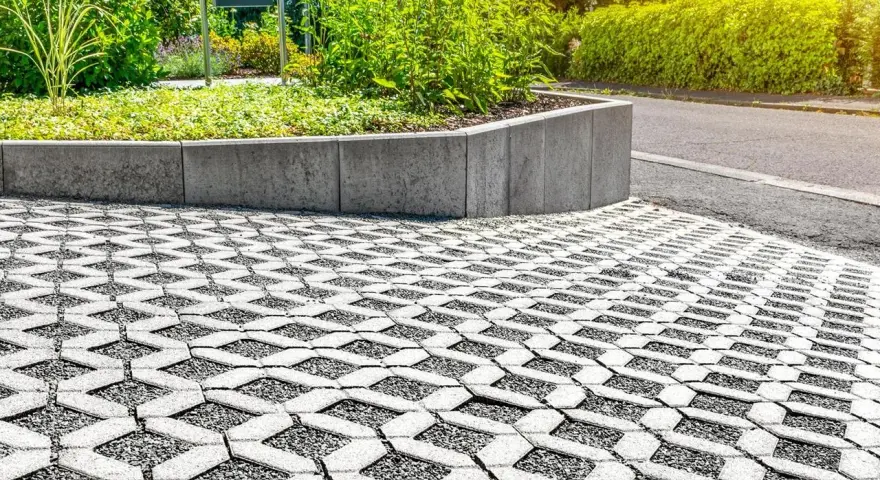 Przestrzeń z ażurową nawierzchnią, która zapewnia minimalną powierzchnię biologicznie czynną, otoczona zielenią i betonowym murkiem.