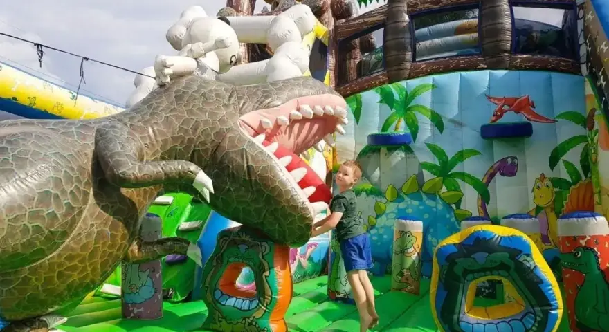 Chłopiec skacze na dmuchanym dinozaurze. Wspaniała atrakcja dla dzieci, jedno z wielu **ciekawe miejsca do 100 km od Katowic**.