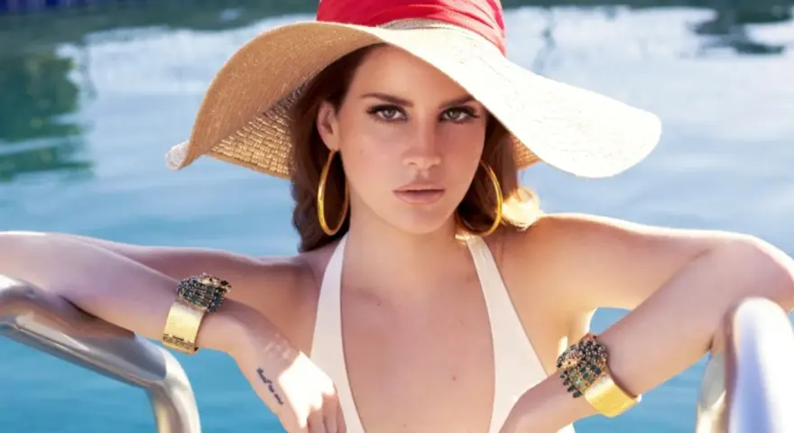 Lana Del Rey, wokalistka, w letnim kapeluszu i biżuterii, relaksuje się przy basenie.
