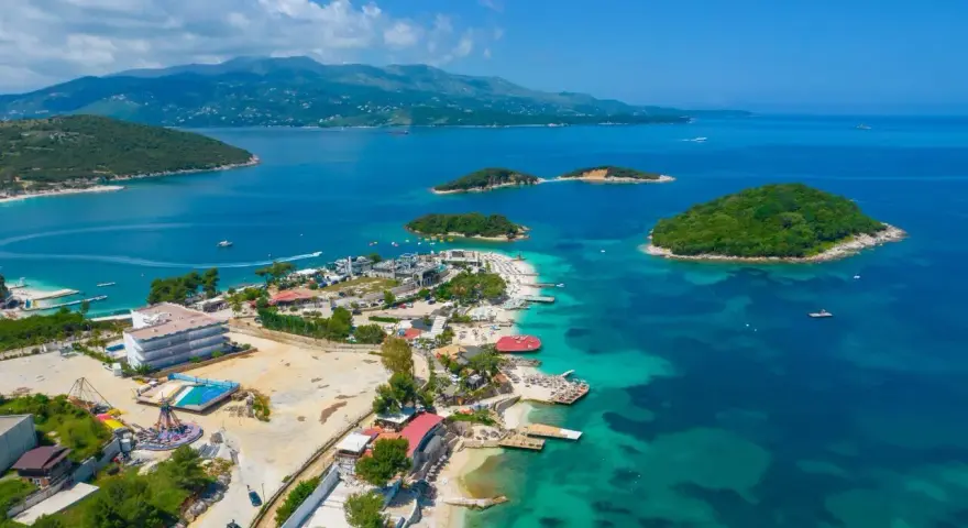 Rajska plaża z wysepkami, idealne miejsce na albania wakacje. Turkusowa woda, hotele i zielone wzgórza tworzą malowniczy krajobraz.