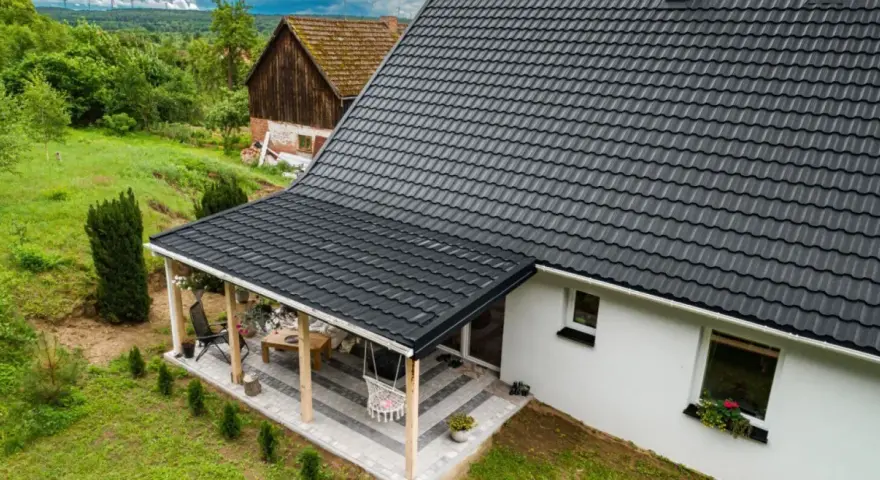 Nowy, czarny dach z blachodachówki nad tarasem i domem. Wymiana dachu zakończona sukcesem, dom zyskał nowy, nowoczesny wygląd.