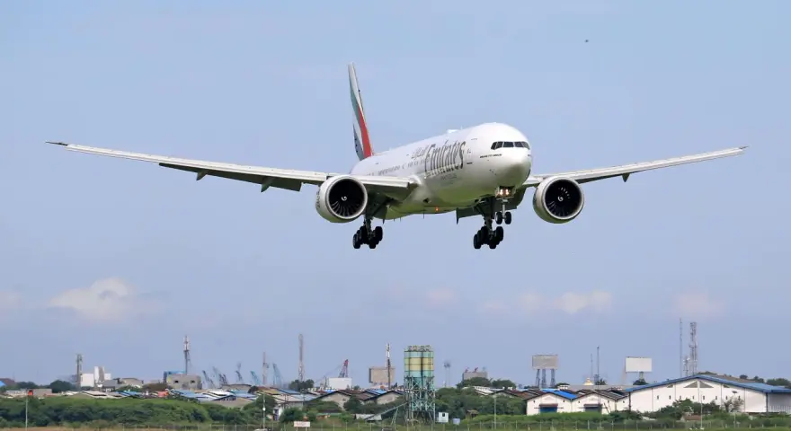 Emirates Boeing 777 zbliża się do lądowania. W tle widać przemysłowy krajobraz i inne samoloty na niebie, sugerujące ruch lotniczy, być może związane z dżerba loty.