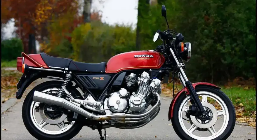 Klasyczny czerwony motocykl Honda CBX 1000 z lat 80. stoi na drodze, otoczony jesienną zielenią i opadłymi liśćmi.