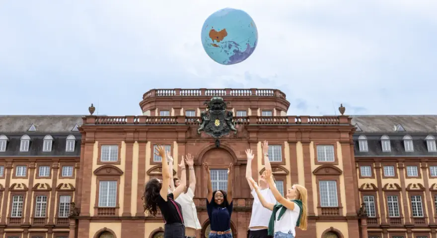 Studierende werfen einen Globus in die Luft vor dem Gebäude des akademischen Auslandsamtes.