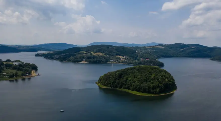 Widok z lotu ptaka na jezioro z wyspą porośniętą lasem i otoczone wzgórzami.