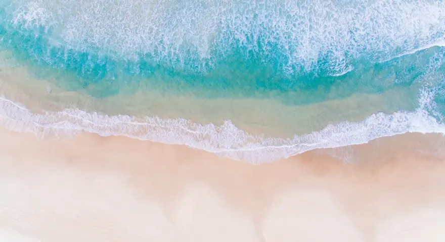 Vue aérienne d'une photo à la plage, avec des vagues turquoise déferlant sur le sable doré.
