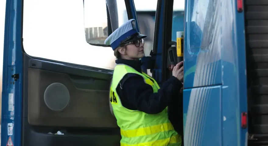 Policjantka w kamizelce odblaskowej i czapce przykłada alkomat do drzwi ciężarówki.