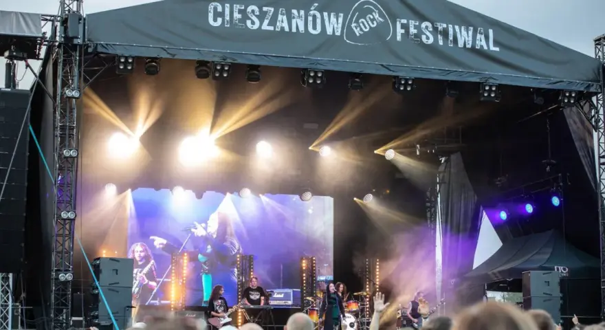 Zespół gra na scenie podczas Cieszanów Rock Festiwal. W tle wielki ekran z wizerunkiem wokalistki i reflektory.