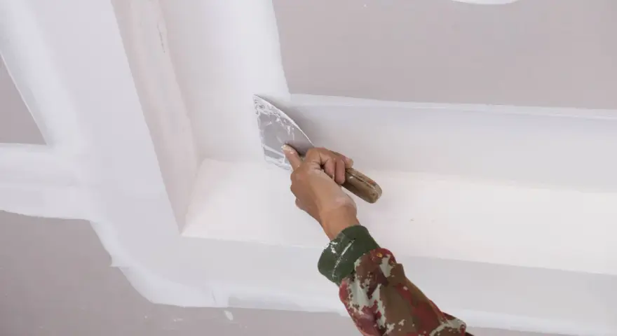 Mano con espátula aplica masilla para pegar escayola rota en el techo.