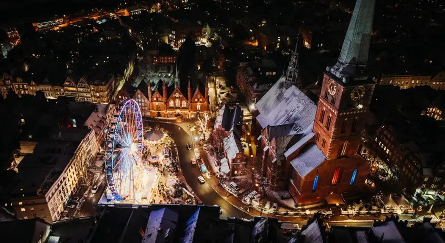 Lichterglanz auf dem Weihnachtsmarkt Schleswig-Holstein: Ein Riesenrad dreht sich neben einer Kirche, während Schneeflocken fallen.