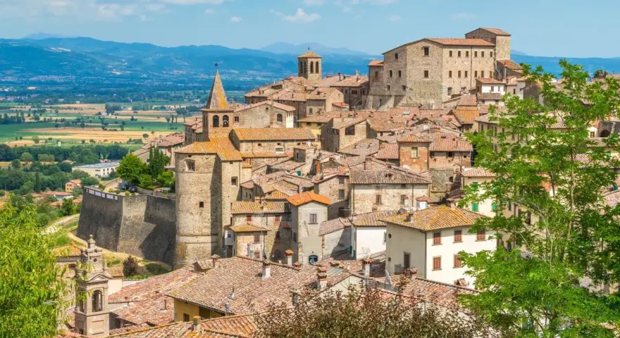 Borgo medievale con tetti in cotto e una torre campanaria, incastonato tra dolci colline verdi. Un luogo che evoca il fascino del **passo dello spino**.