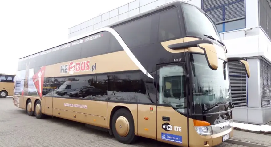 Złoty dwupiętrowy autokar Neobus.pl zaparkowany przed budynkiem.
