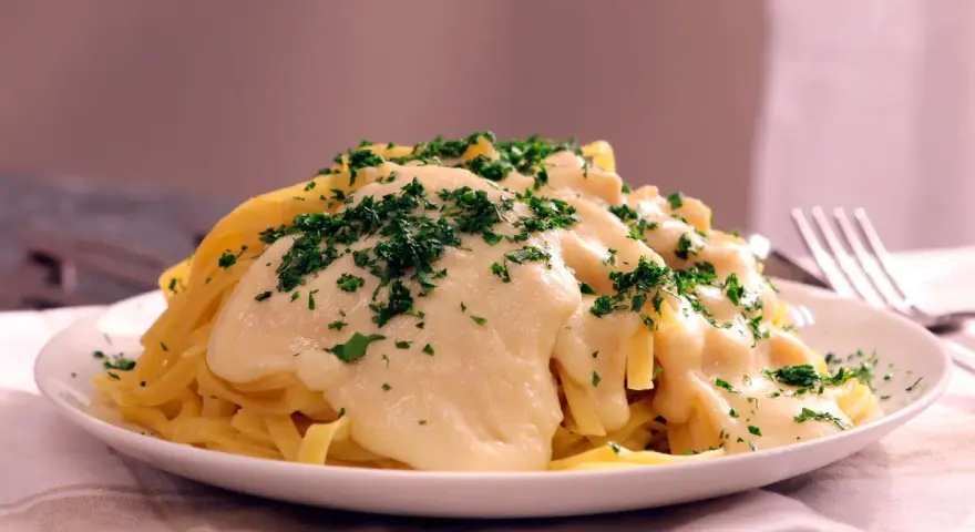 Pasta Alfredo cremosa con perejil picado en un plato blanco.
