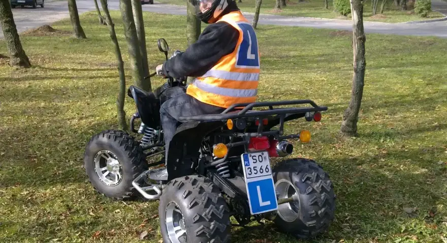Mężczyzna w kasku i kamizelce odblaskowej siedzi na quadzie z literą L. Zastanawiasz się, jakie prawo jazdy na quada jest potrzebne?