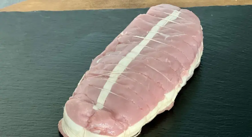 Rôti de veau cru ficelé, prêt à cuire, sur une planche sombre.