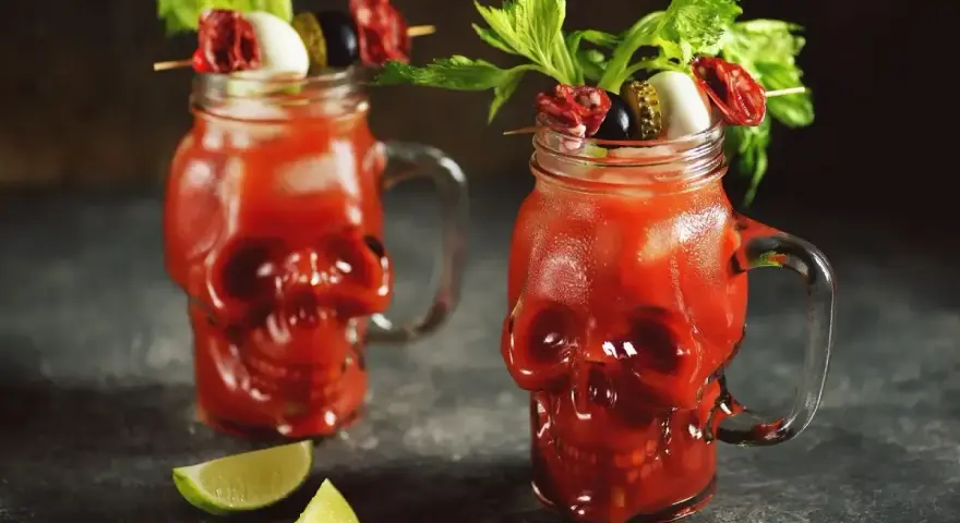 Dwa krwawe drinki ze spirytusem w szklankach w kształcie czaszek, udekorowane łodygami selera, oliwkami i plasterkami salami.