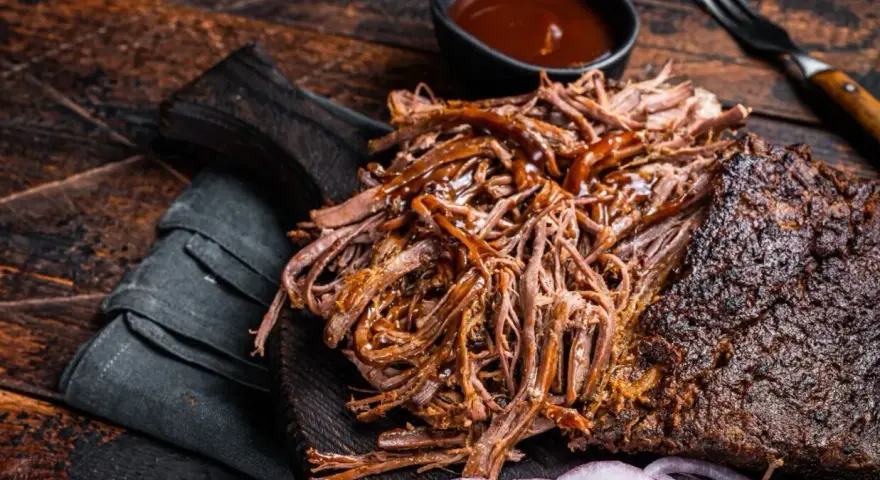 Soczysta, aromatyczna szarpana wołowina, polana sosem BBQ, podana z krążkami cebuli na drewnianej desce. Idealna na grilla.