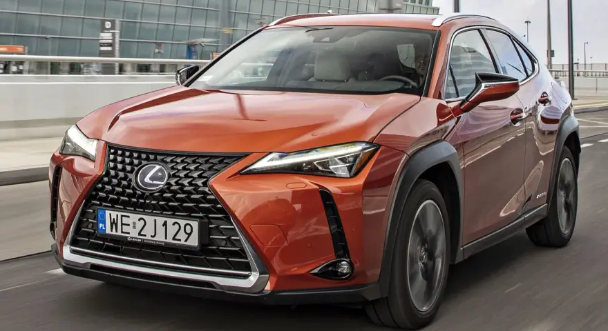 Pomarańczowy Lexus UX 250h w ruchu miejskim, z nowoczesnym grillem i reflektorami LED.