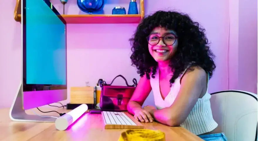 Giovane donna sorridente al computer, pronta a diventare e-commerce manager. Sul tavolo, un metro da sarta giallo.