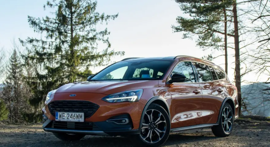 Pomarańczowy Ford Focus kombi na tle drzew i nieba.